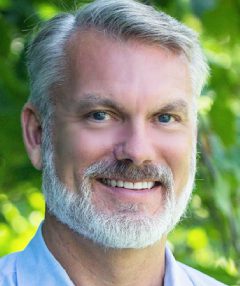 A man with grey hair and beard smiling for the camera.