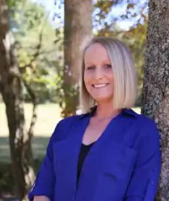 A woman standing in front of a tree smiling for the camera.